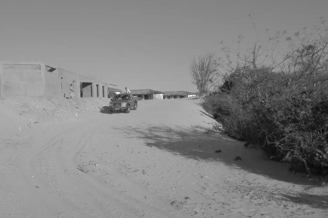 A black-and-white image of a dirt road with a parked car