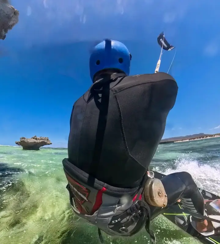 A kitesurfer in a blue helmet rides over green waves