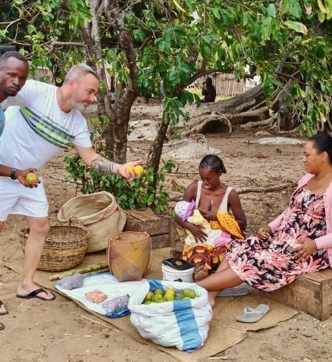 A man hands fruit to a woman sitting with a baby