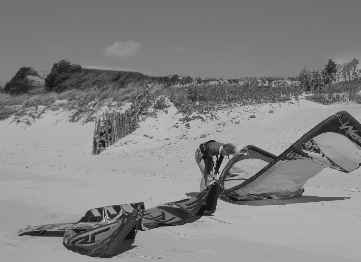 A person in a wetsuit adjusts a colorful kite on a sandy beach