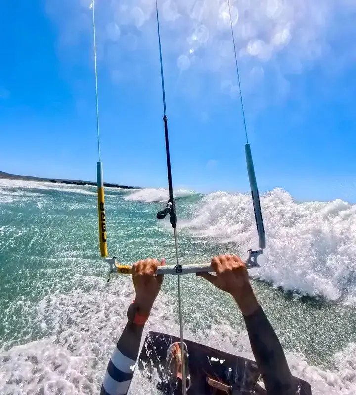 Kitesurfer controlling bar over turquoise waves.